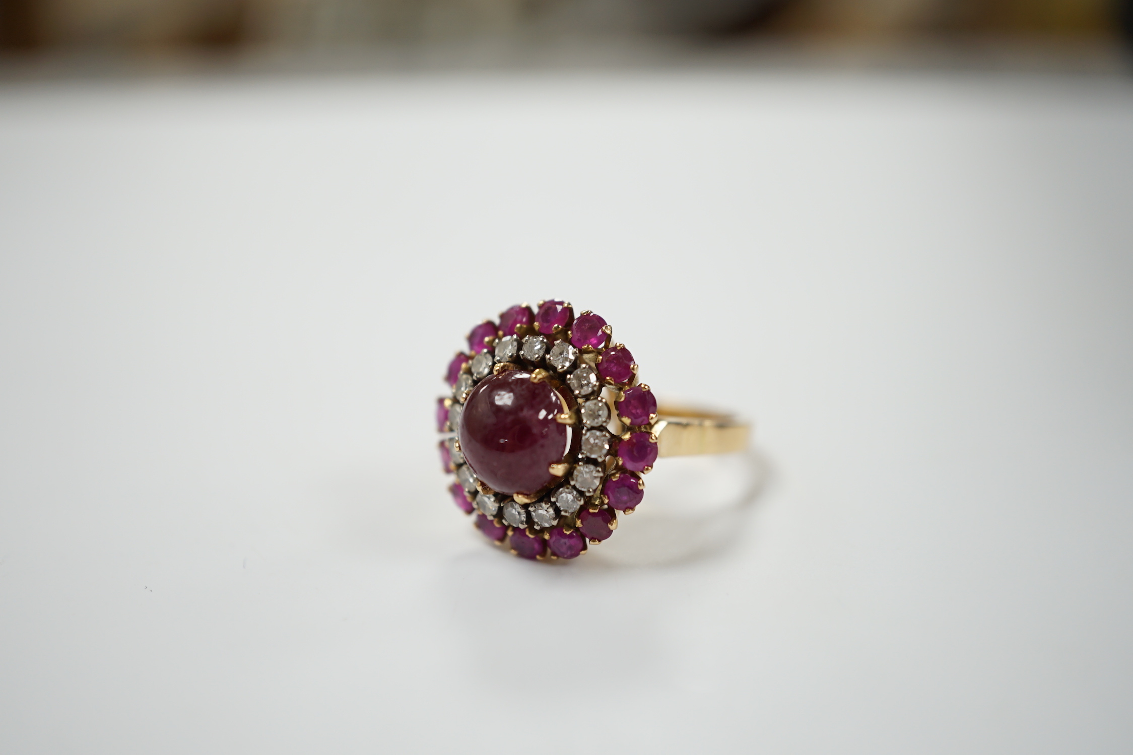 A yellow metal, ruby and diamond set circular cluster dress ring, with central cabochon ruby, size M/N, gross 8.2 grams.